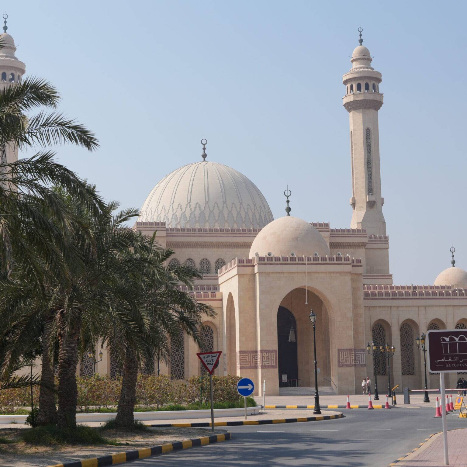 Moschee mit großen Kuppeln und Minaretten, umgeben von Palmen und einer Straße im Vordergrund.