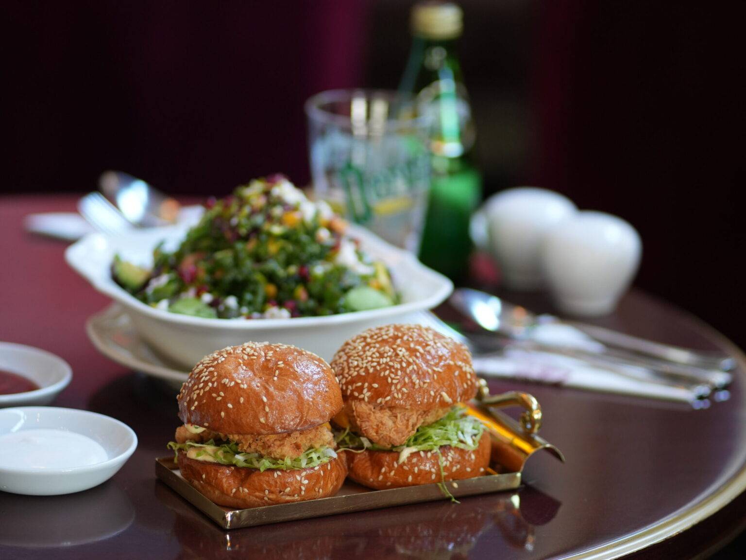 Ein gedeckter Tisch mit zwei Mini-Burgern auf einem goldenen Tablett im Vordergrund.