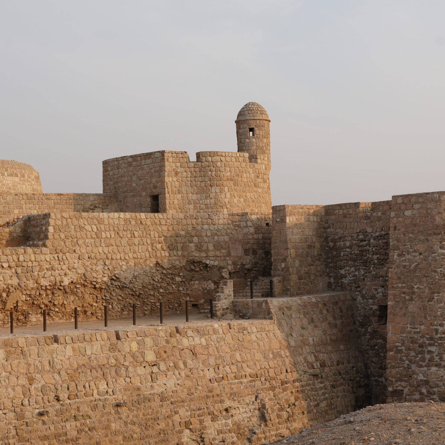 Historische Steinmauer mit Türmen und verschiedenen Höhen, unter einem hellen Himmel.