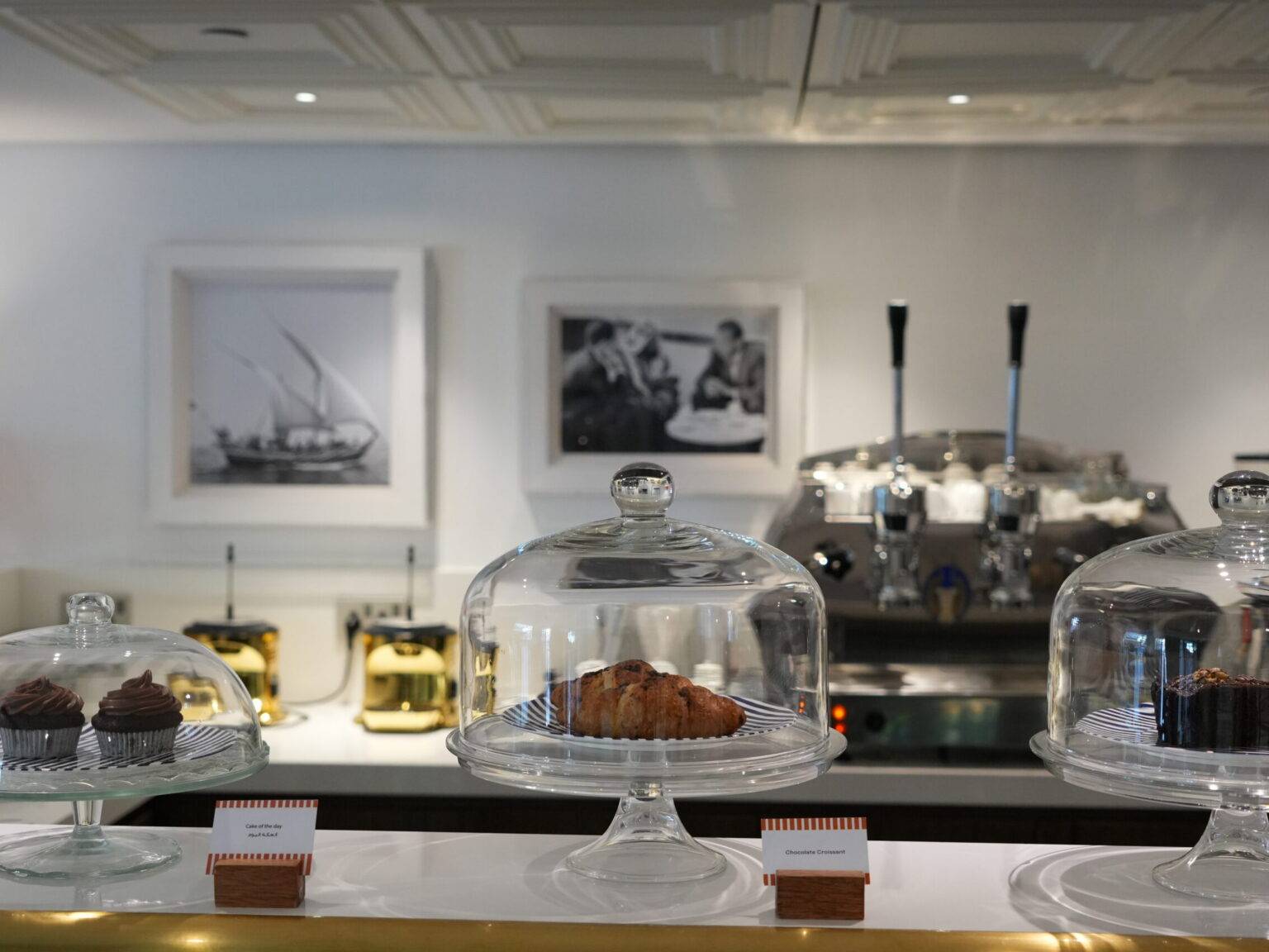 Vitrine mit Kuchen und Gebäck, im Hintergrund eine Kaffeemaschine und Schwarz-Weiß-Fotos an der Wand.