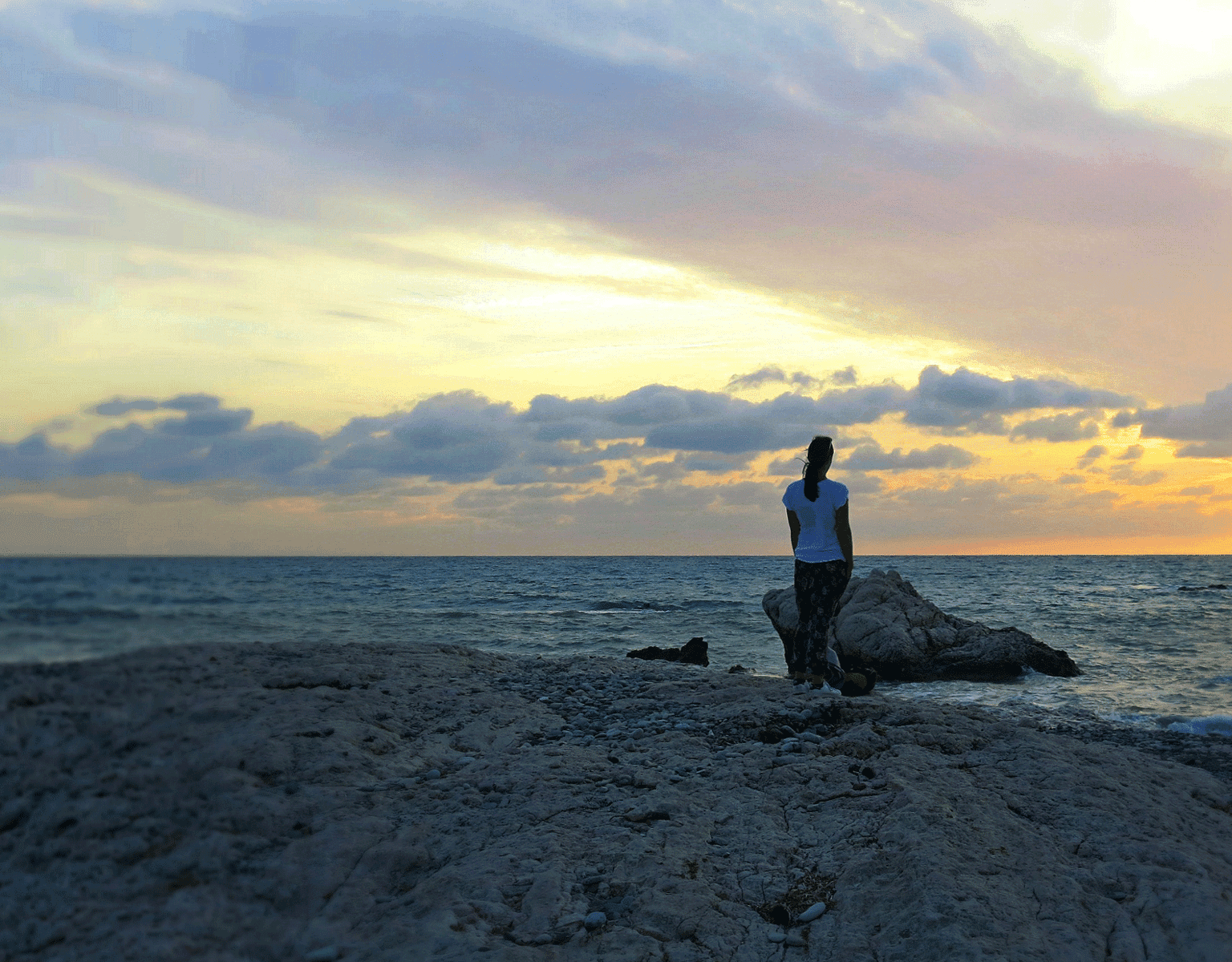 Reisebloggerin Eva genießt am Aphrodite-Strand Petra tou Romiou in Zypern den Sonnenuntergang über dem Meer.