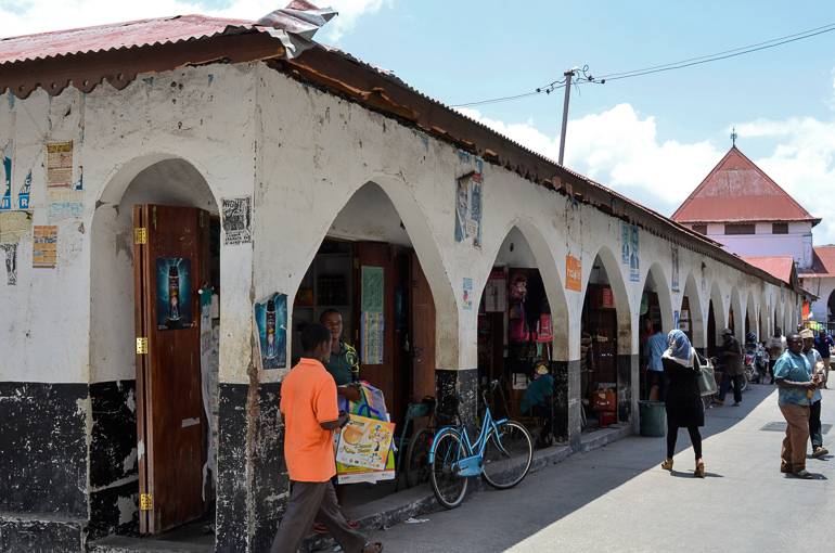 Auf Sansibars Darajani Markt in Stonetown kann man sich in Läden, die sich hinter Torbögen einer langen Häuserfront verbergen Artikel des täglichen Bedarfs erwerben.