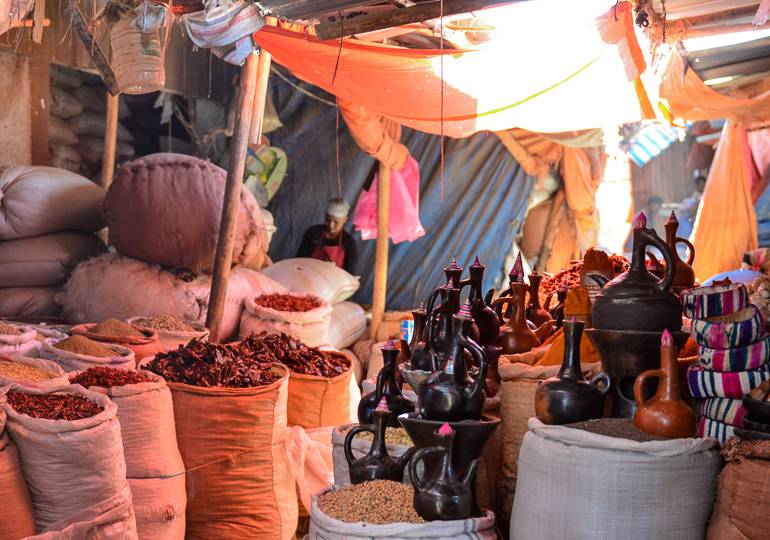 Auf einem Marktplatz in Harar, Äthiopien, werden unter Stoffsegeln Gewürze in großen Säcken und Öle in Tonkännchen verkauft.
