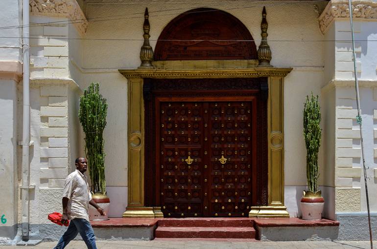 Ein verziertes Tor aus dunklem Holz und goldenem Rahmen schmückt den Eingang eines Hauses auf Sansibar.