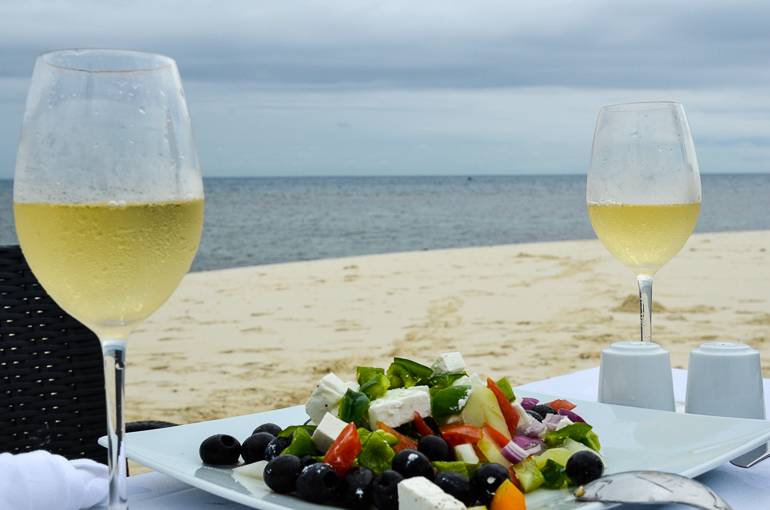 Bei einem romantischen Dinner amStrand von Sansibar wurden 2 Gläser Weißwein und ein Salat auf dem Tisch angerichtet.