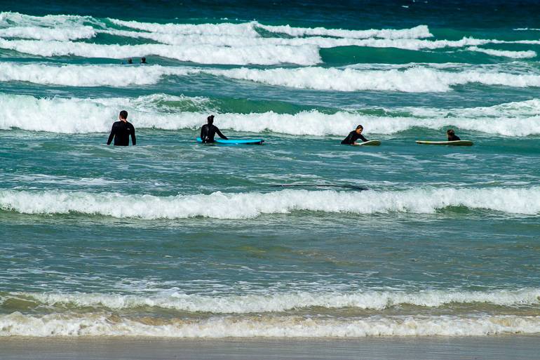 In der Südafrikanischen Kapregion Muizenberg Beach warten vier Surfer im Meer auf eine Welle.