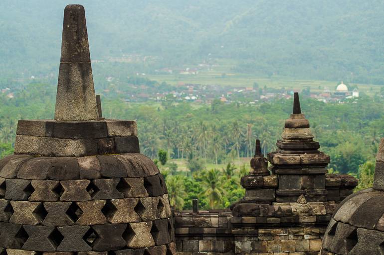 Über die Glocken des Tempels hinweg breitet sich die grüne Landschaft Javas aus.
