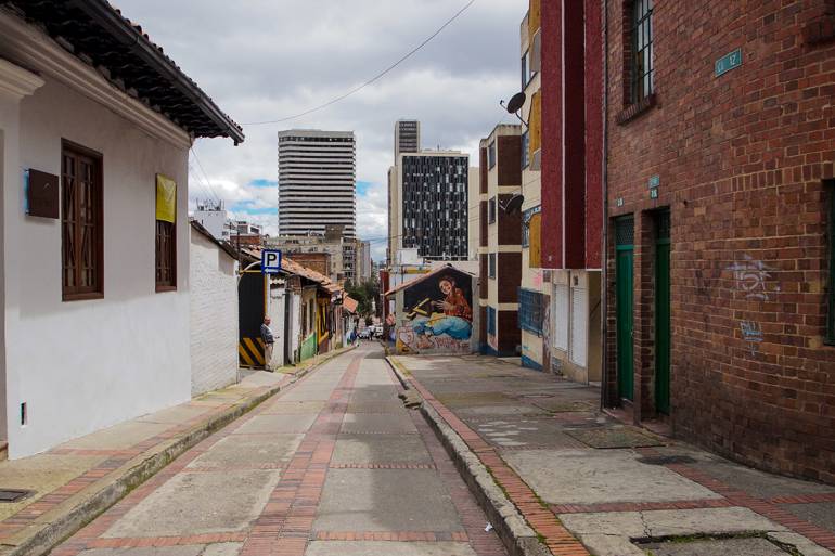In einer kleinen Gasse in Bogotás Viertel La Candelaria geht es bergabwärts vorbei an mit Graffiti verzierten Häuserwänden und Hochhäusern.