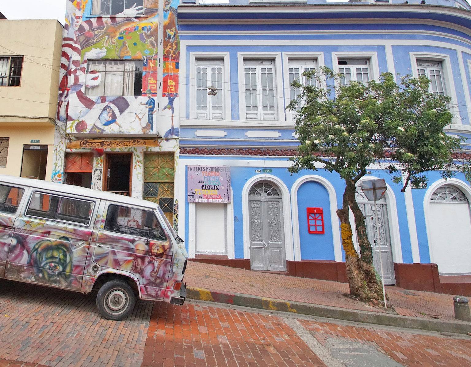Ein bunt besprühter VW-Bus steht in den Straßen von Kolumbiens Hauptstadt Bogotá. Im Hintergrund sieht man Graffiti an der Hausfassade.
