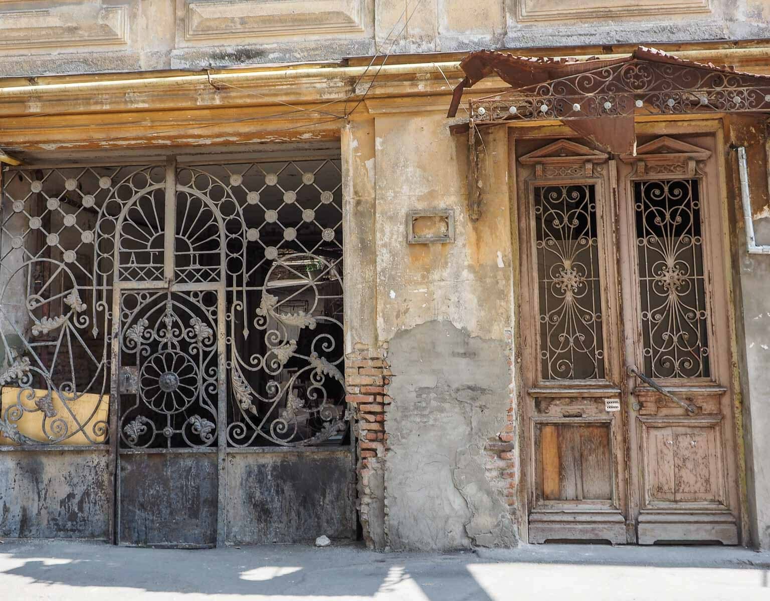 Eine bröckelnde Hausfassade mit altem verziertem Eisentor und Holztür ziert eine Straße von Tiflis Wohngegend Sololaki in Georgien.