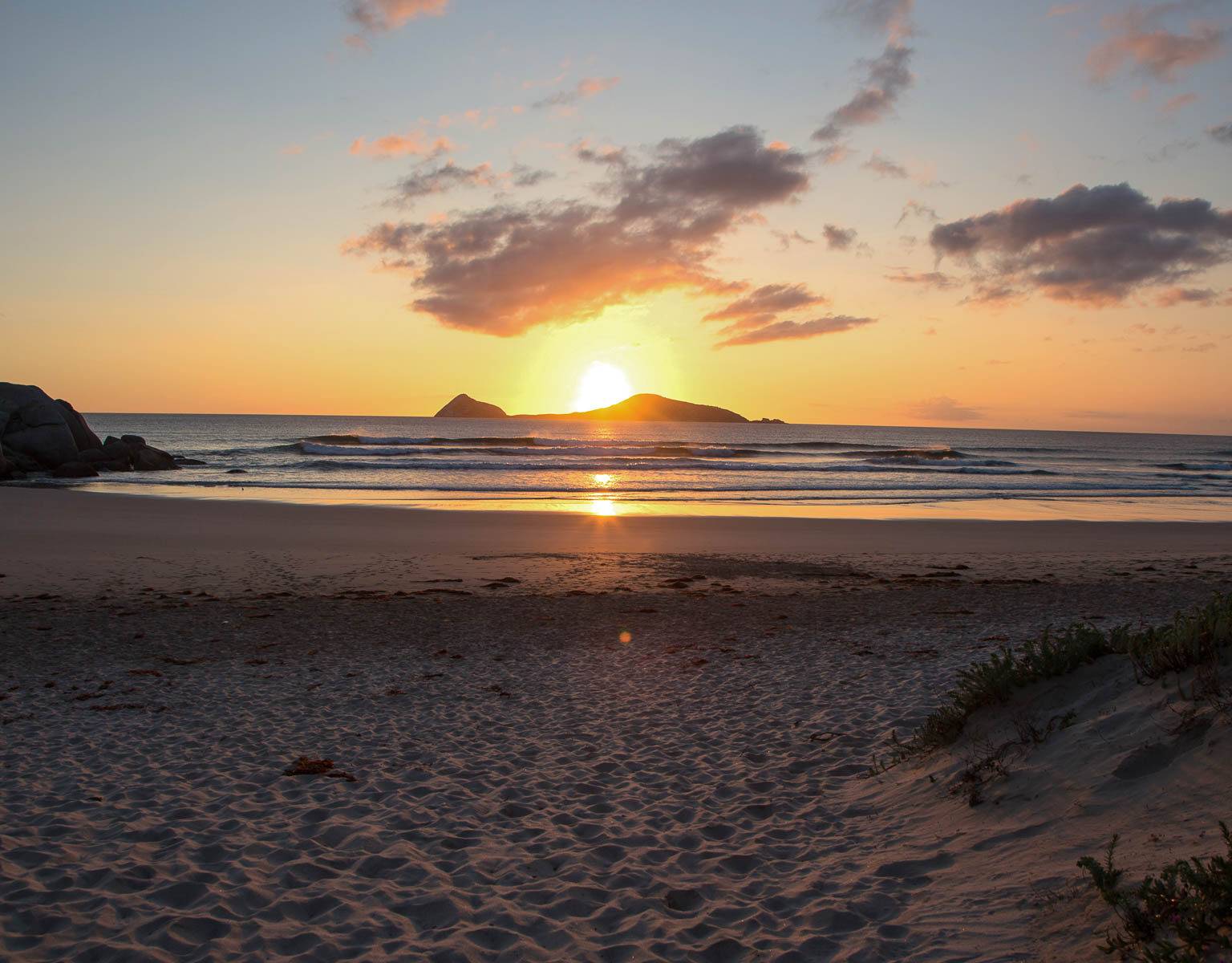 Vom Strand im australischen Bundesstaat Victoria aus sieht man am Horizont die Sonne im Meer versinken.