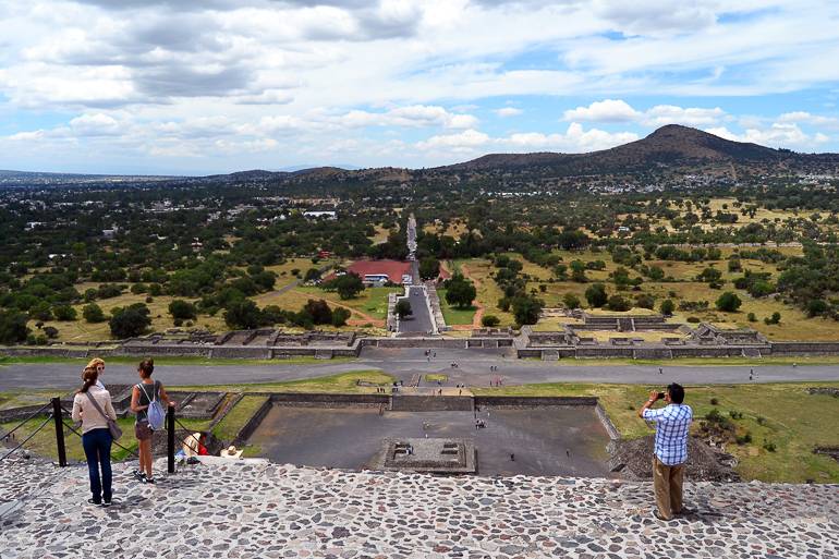 Touristen stehen auf einer Aussichtplattform einer Pyramide und blicken in die mexikanische Landschaft von Teotihuacan.