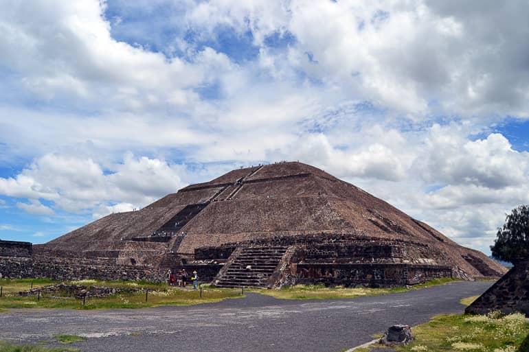 Mexikos steinerne Sonnenpyramide mit ihren zahlreichen Treppenstufen ist von grünen Wiesen umgeben.