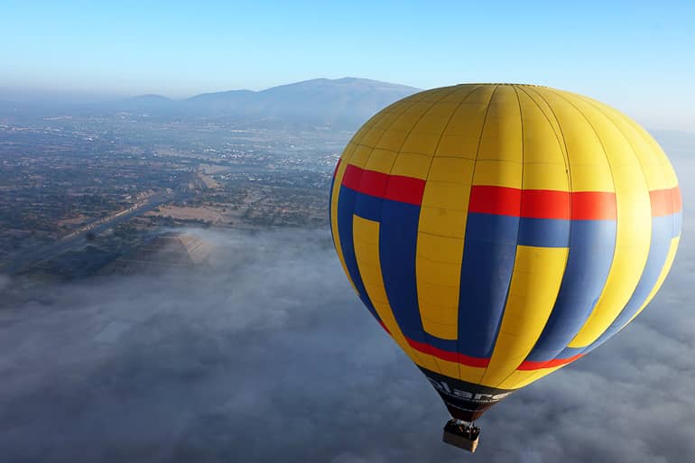Ein gelber Heißluftballon mit blau-rotem Muster fliegt über die Pyramiden von Teotihuacan, Mexiko.