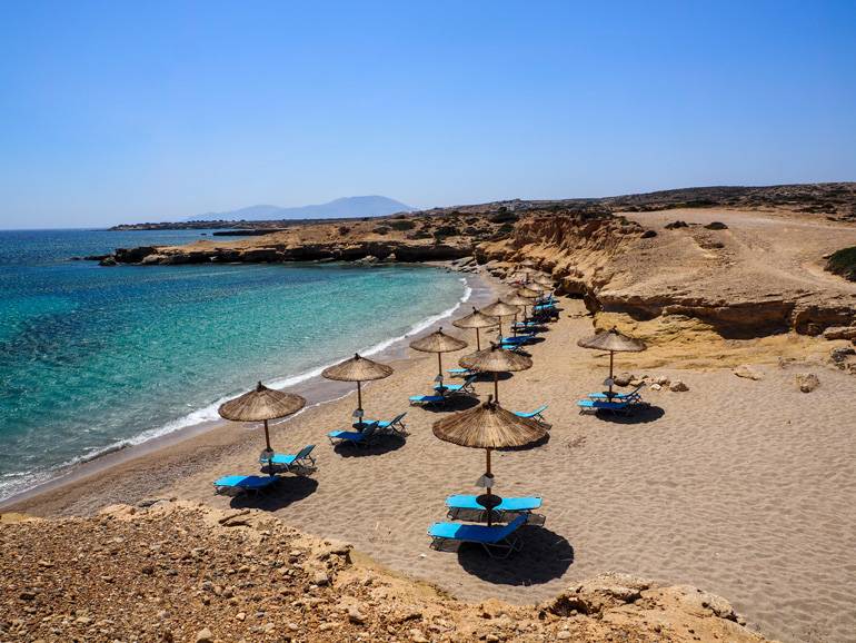 Am wunderschönen Michalioú Kipos Strand zieren Strohschirme und blaue Liegen den malerischen Ausblick aufs Meer.