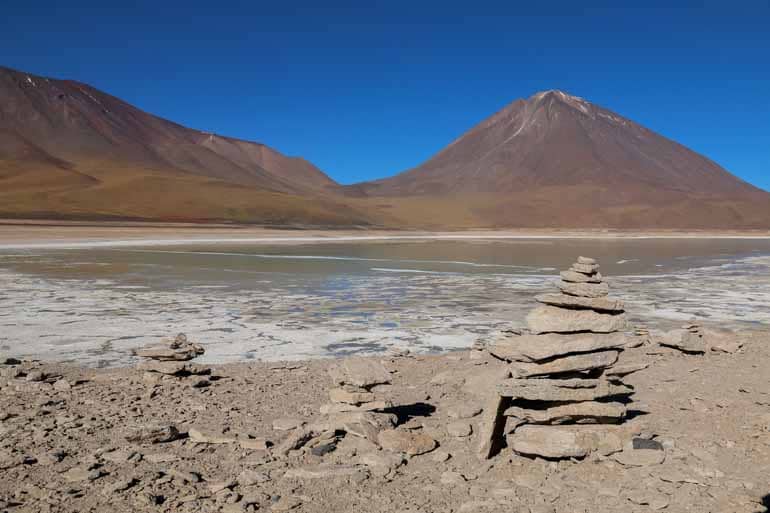 Ein Steinplattenturm mit Lagune und Berg im Hintergrund kann man bei einer Lagunentour in Bolivien bestaunen.