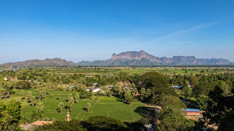 Myanmar: Aussicht von oben auf die grüne Landschaft von Hpa An, im Hintergrund sind Berge zu sehen.