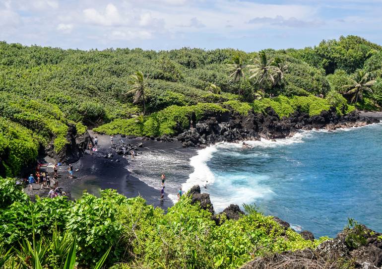 Der Waianapanapa Beach auf Maui Hawaii ist berühmt für seine schwarze Sandfärbung, eine grüne Naturlandschaft rahmt ihn ein.