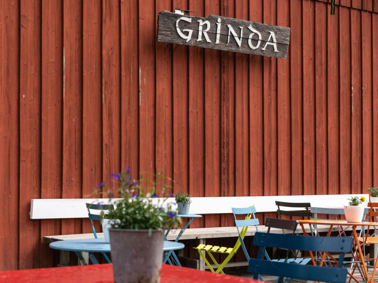 Bunte Stühle und Tische warten vor dem Grinda Lanthandel Café mit seiner roten Holzfassade auf Gäste.