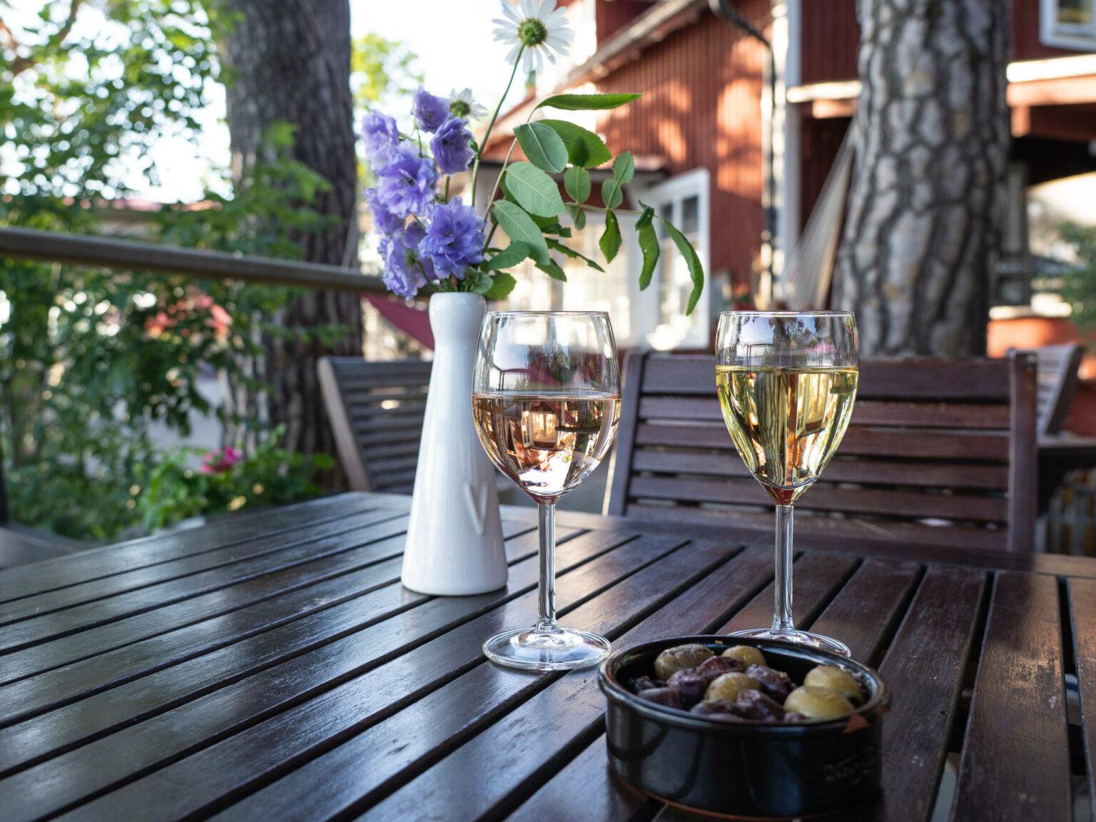 Zwei Gläser Wein und ein Schälchen Oliven stehen auf einem Holztisch im gemütlichen Außenbereich des Restaurants Röda Villan auf Fjäderholmarna.