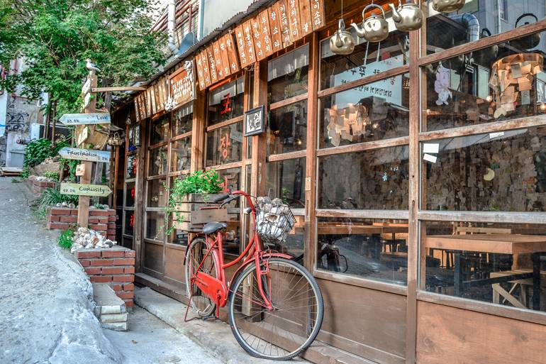 Seoul Sehenswürdigkeiten: In einem Holzhaus befindet sich ein Restaurant, davor lehnt ein rotes Fahrrad.
