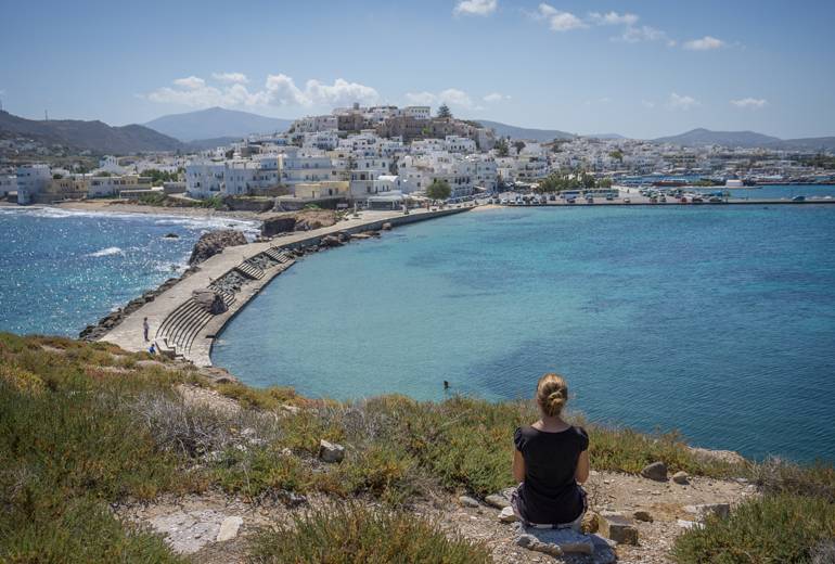 Eine Frau sitz am Boden von einem Aussichtspunkt und schaut auf das Meer und die Stadt hinunter.