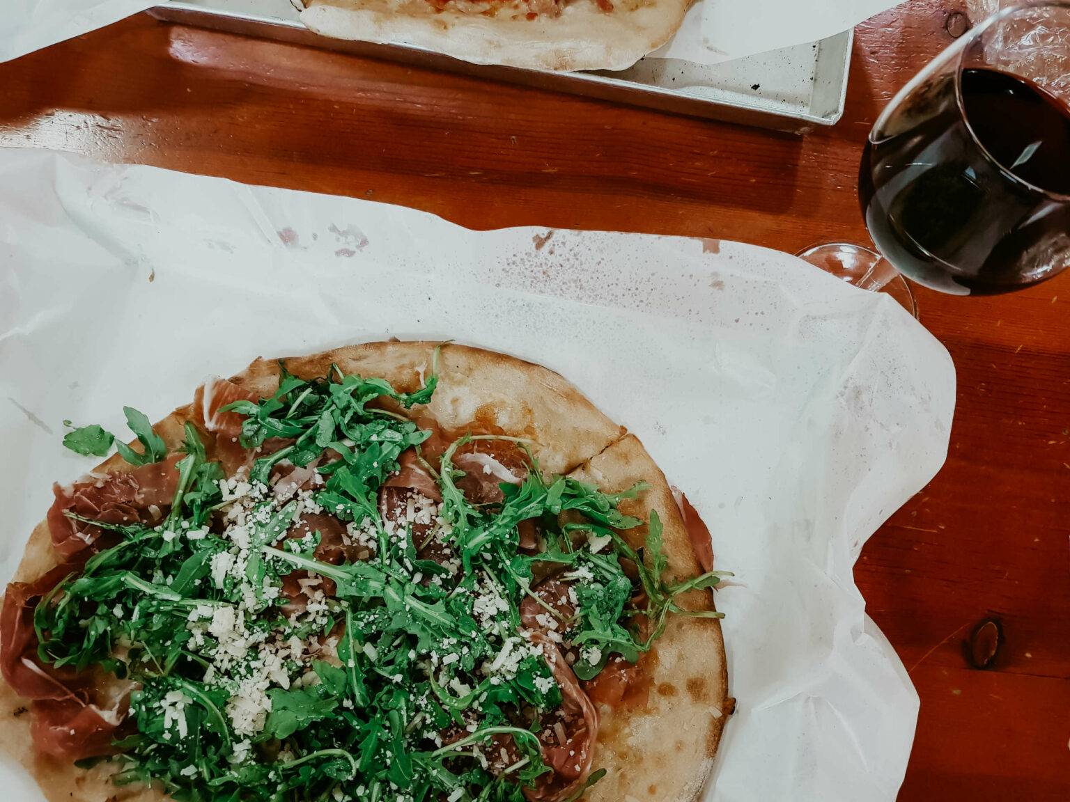 Eine Pizza mit einem Glas Rotwein daneben.