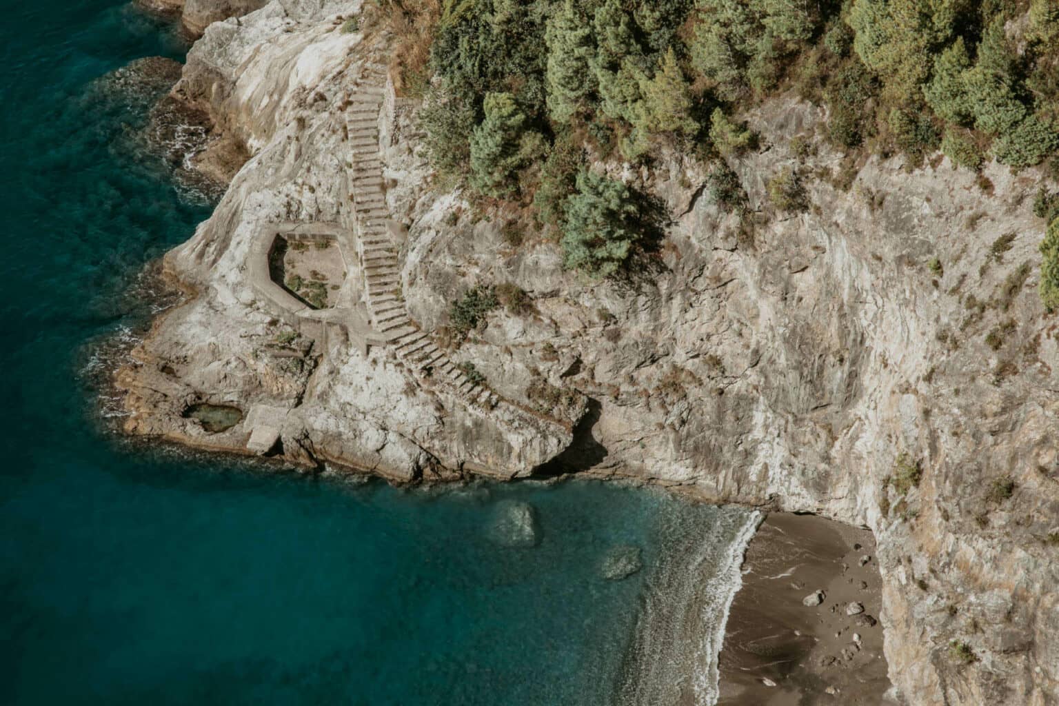 Ein kleiner Strand von oben, zu dem eine lange Treppe vom Berg hinunter führt.