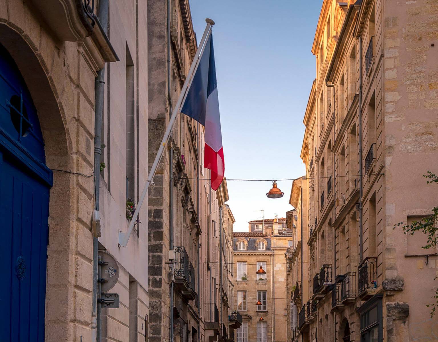 Französische Flagge an einer Häuserwand in einer engen Gasse in Bordeaux, davor eine blaue Tür