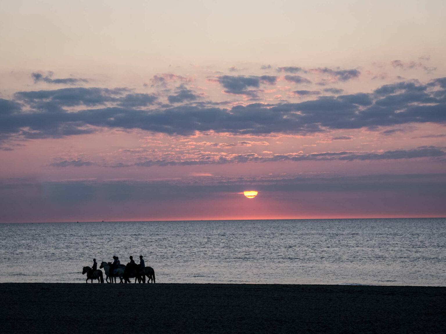 Sonnenuntergang am Meer, Reiter reiten den Strand entlang