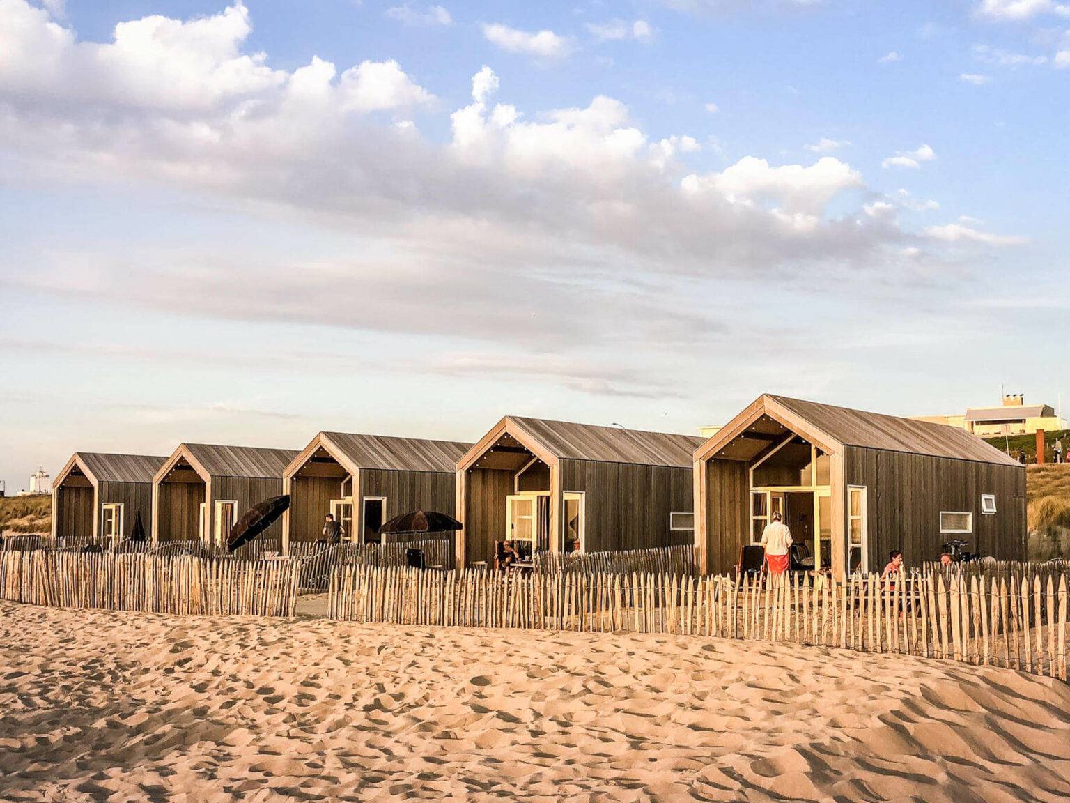 Sandstrand und fünf gleichaussehende Strandhäuser aus Holz nebeneinander in Katwik aan Zee in den Niederlanden