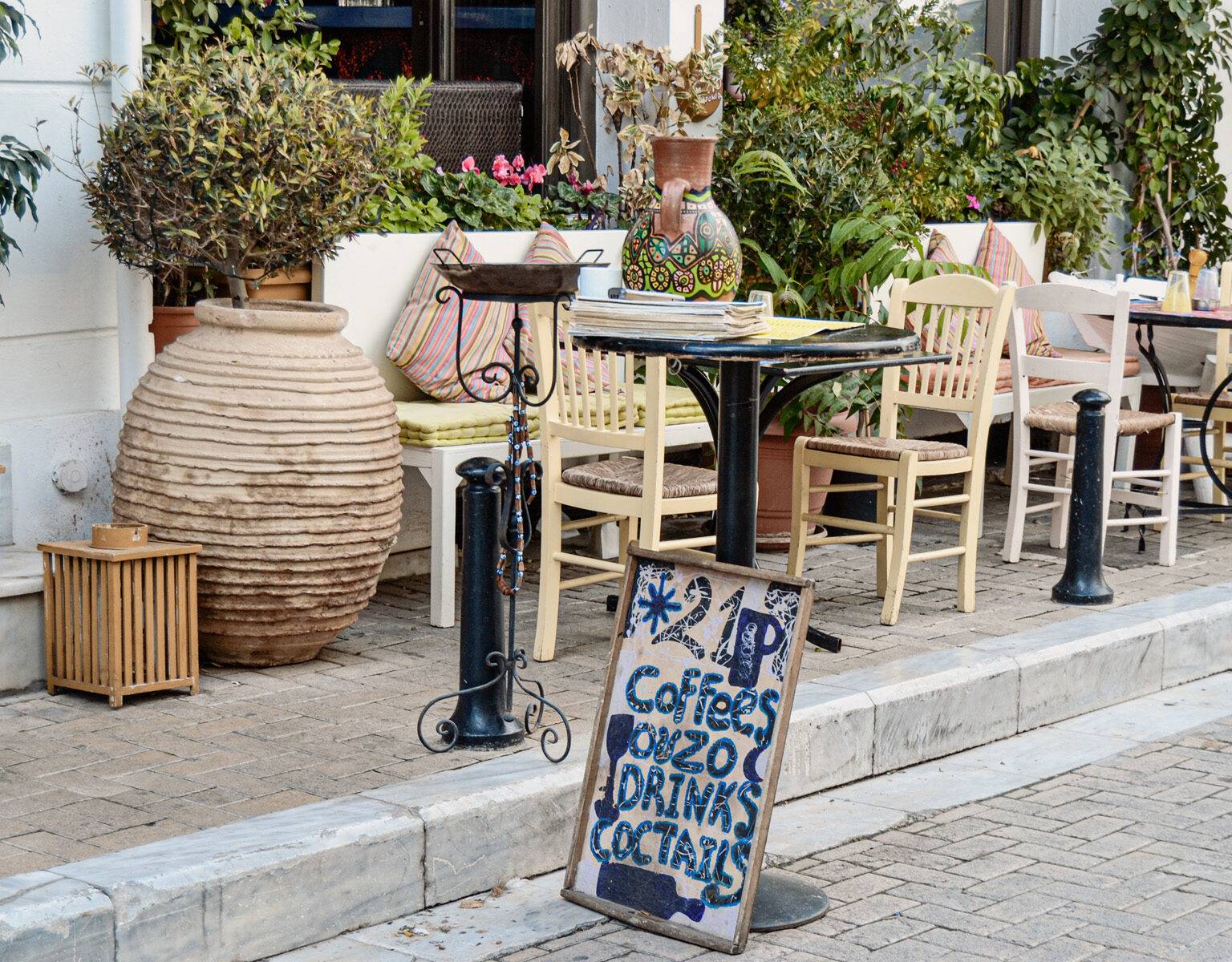Athens kulinarische Seite erkunden: Außenterrasse eines Cafés im Stadtteil Plaka mit einladenden kleinen Stühlen und Tischen.