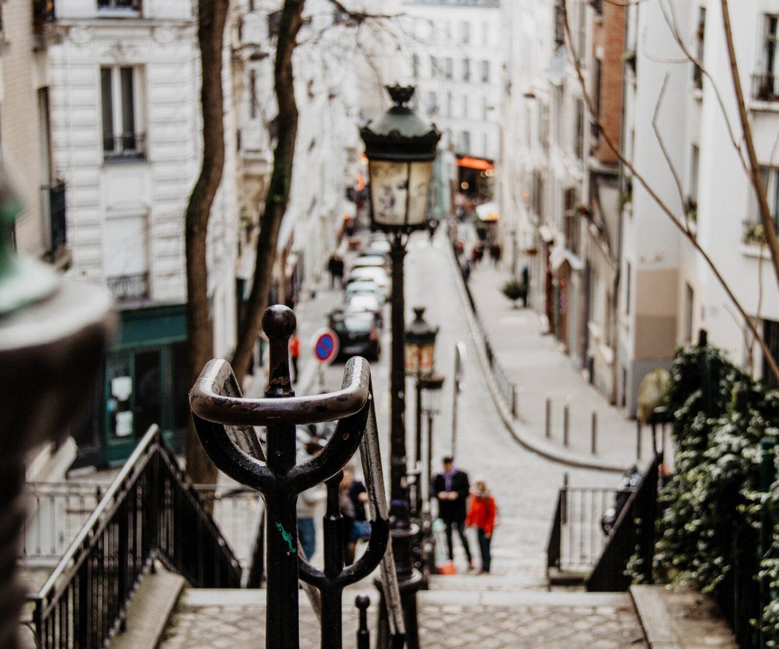 Treppenstufen führen auf den Montmartre, im Hintergrund eine der kleinen, einladenden Gassen von Paris.