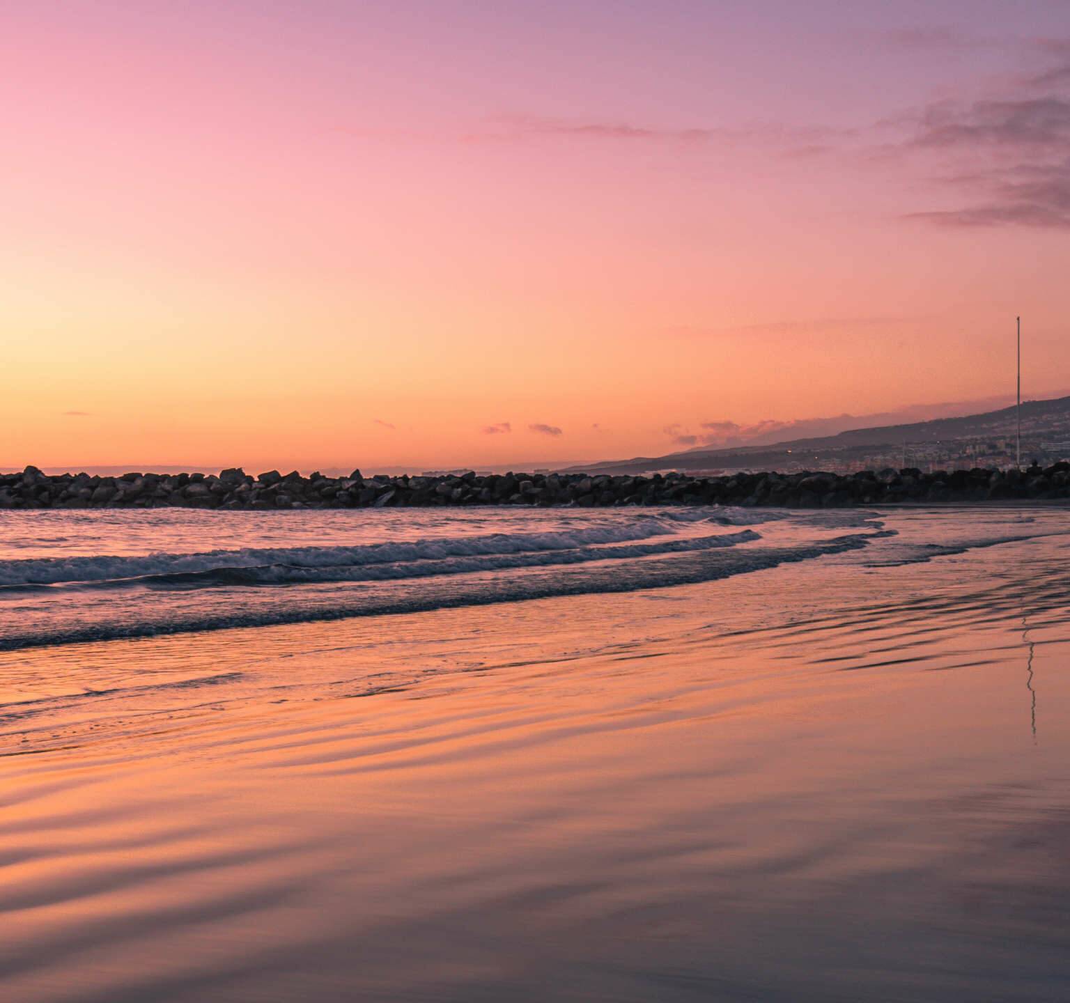 Ein unvergessliches Erlebnis auf Teneriffa: Zum Sonnenuntergang färbt sich der Himmel über dem Strand von Playa de Las Americas in den schönsten Rottönen.