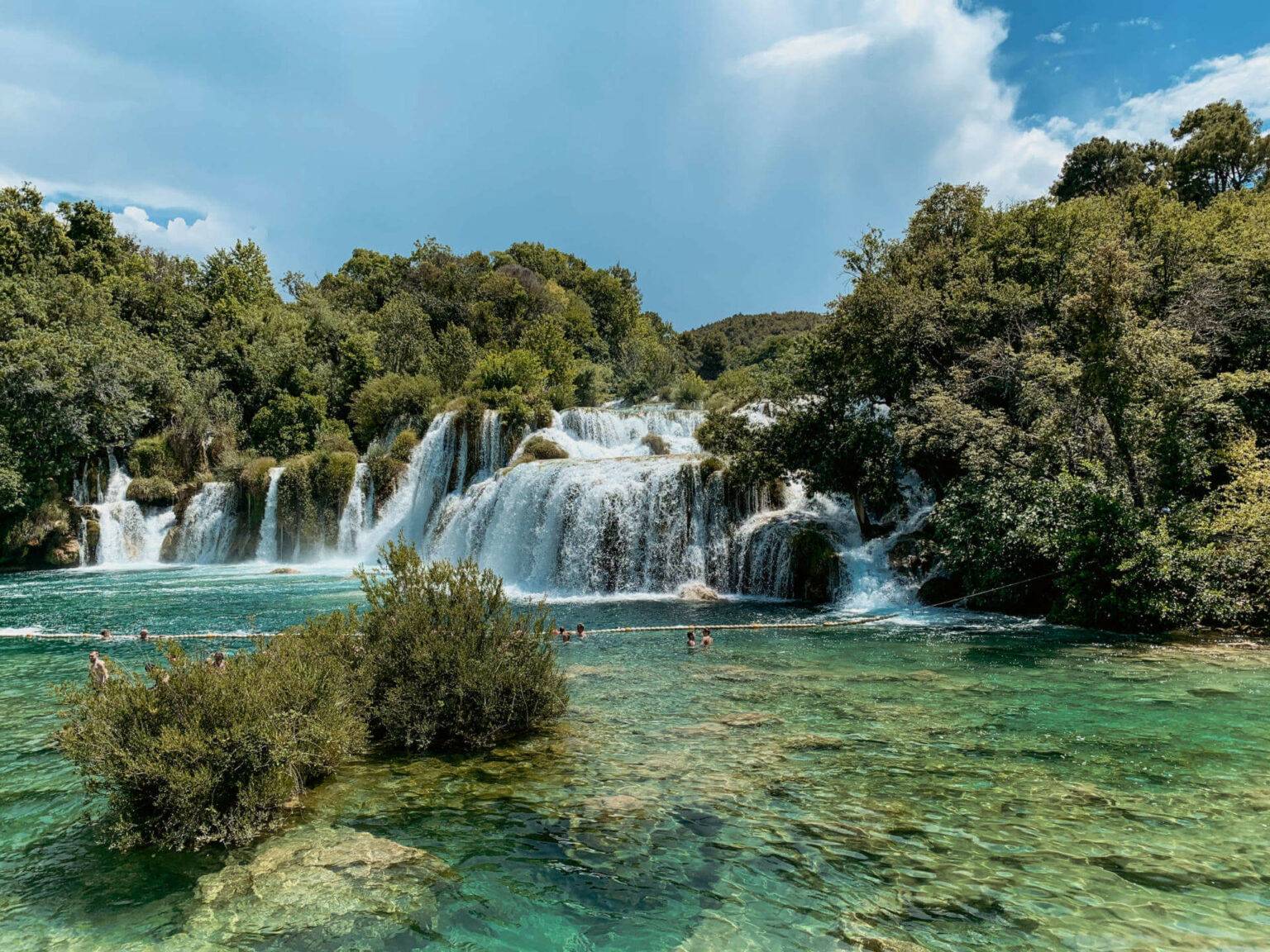 Hier muss man auf einem Roadtrip durch Kroatien einen Stopp einlegen: Der beeindruckende Wasserfall Skradinski Buk in Kroatien. In den Gumpen unterhalb des Wasserfalls schwimmen Besucher.