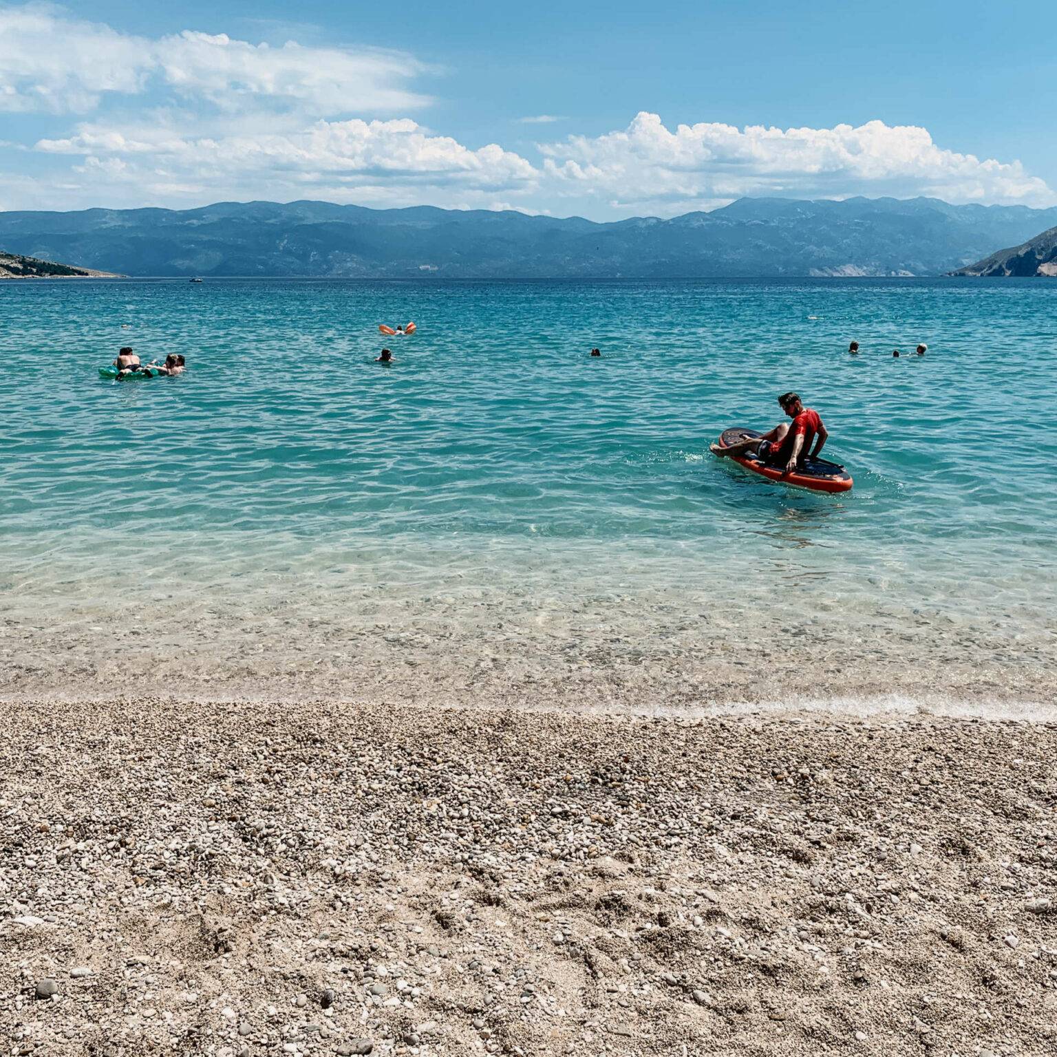 Blick vom Sandstrand Vela Plaža aufs Meer in Kroatien. Auf und in dem Wasser sind viele Wassersportler und Schwimmer unterwegs.