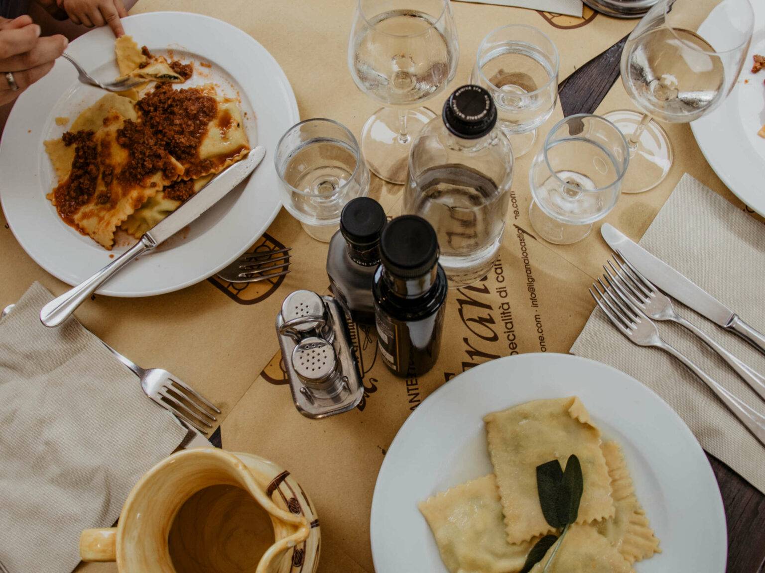 Ein gedeckter Tisch mit italienischen Pasta-Spezialitäten auf weißen Tellern, dazu gibt es italienischen Weißwein.