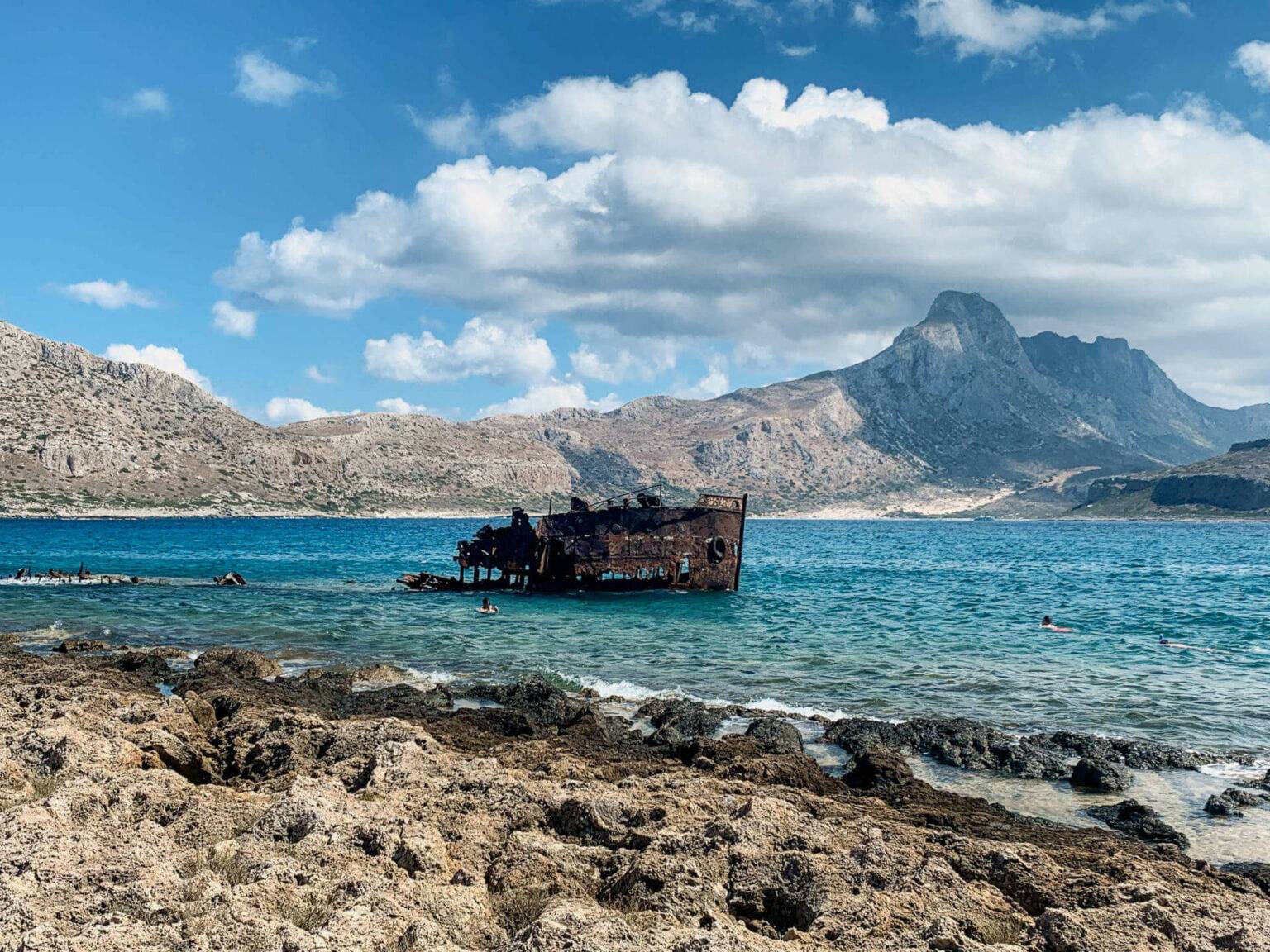 Geheimtipp auf Kreta: Das verrostete Schiffswrack auf der Pirateninsel Gramvousa liegt auf türkisblauem Wasser, im Hintergrund erheben sich die Berge der Insel.