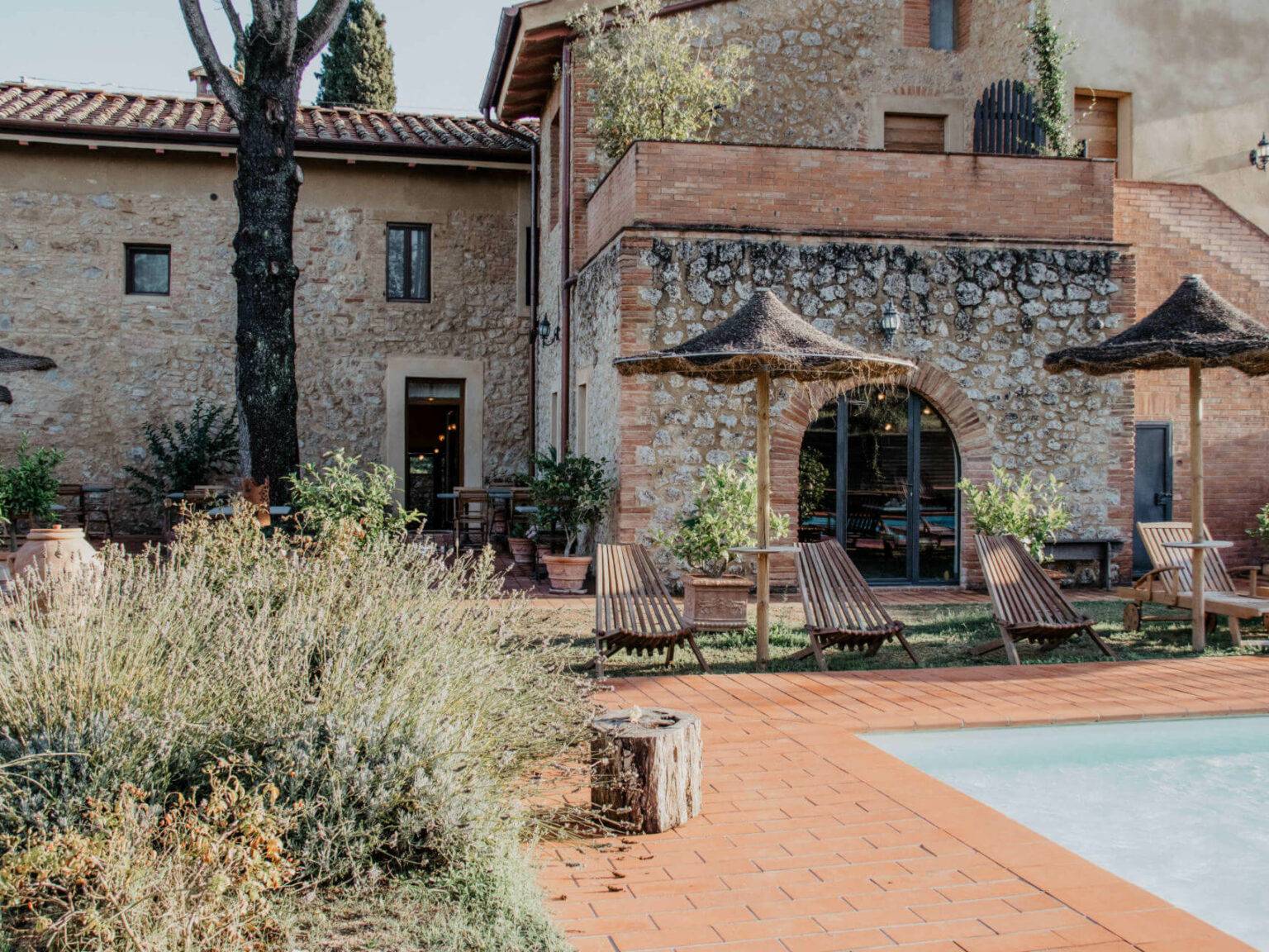 An dem von roten Pflastersteinen umrandeten Pool der Unterkunft Agrivilla i Pini im Herzen der Toskana stehen Liegestühle und Sonnenschirme für die Urlauber bereit.