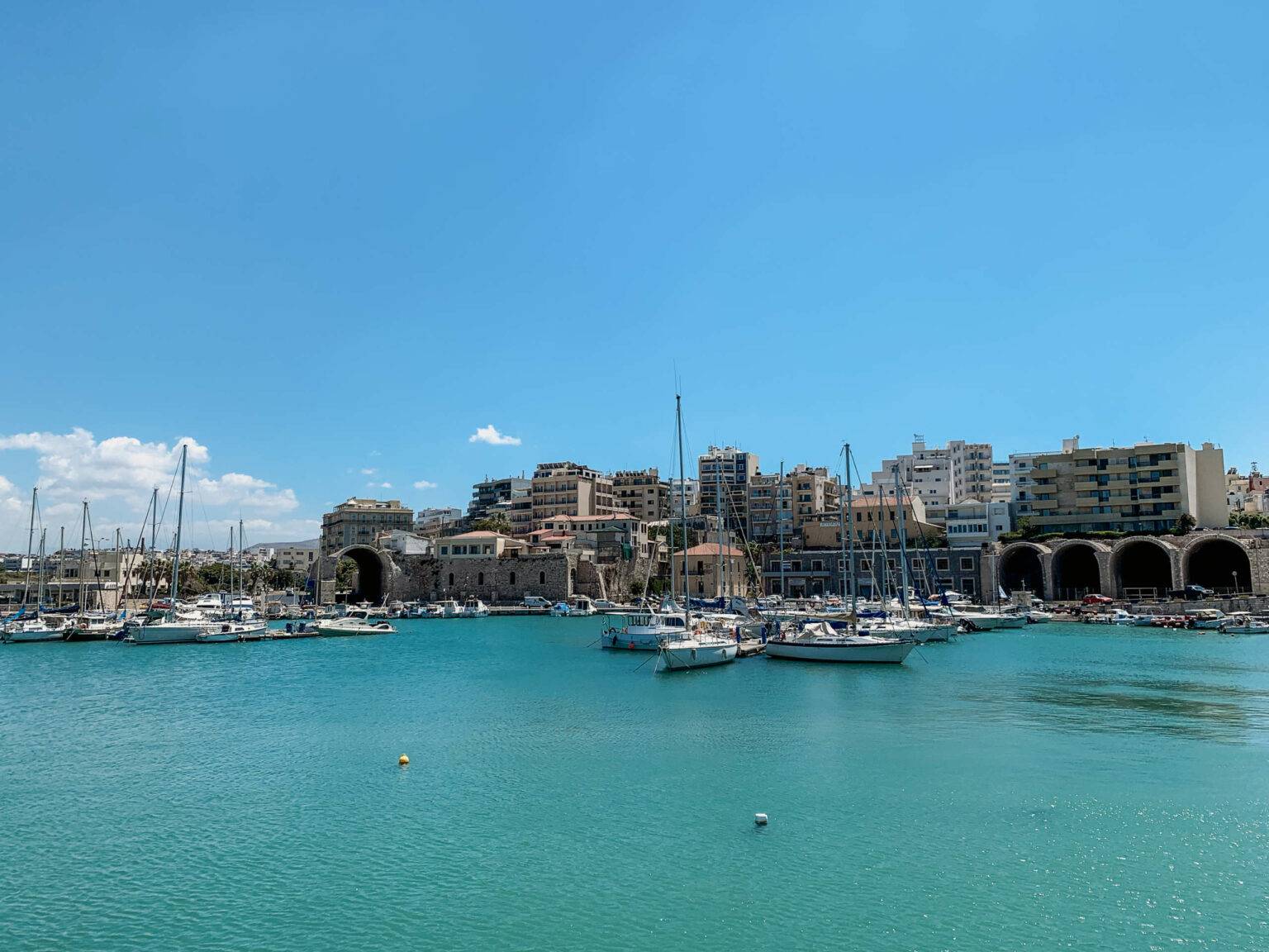 Zahlreiche Boote liegen im Hafen von Heraklion, der Hauptstadt von Kreta. Hinter dem Hafen stehen einige Hochhäuser.