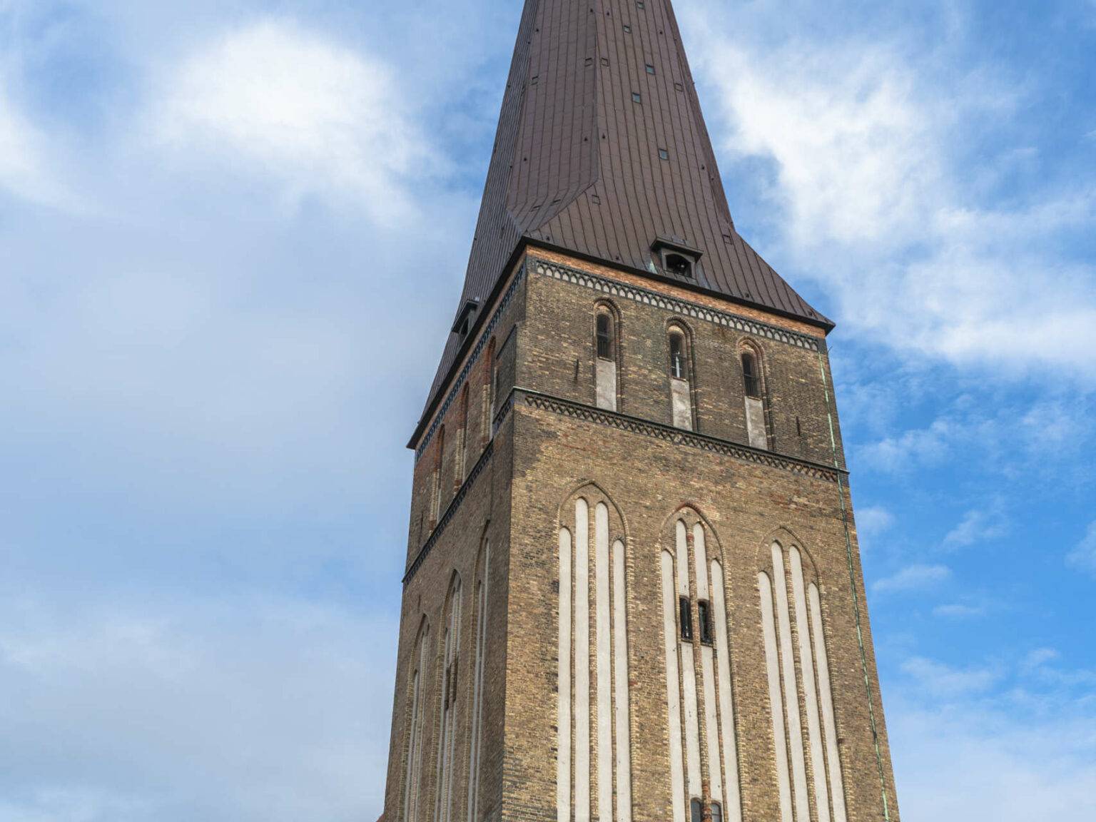 Die Rostocker Petrikirche erhebt sich in den strahlend blauen Himmel mit weißen Wolken, die braunen Backsteine sieht man aus der Froschperspektive.