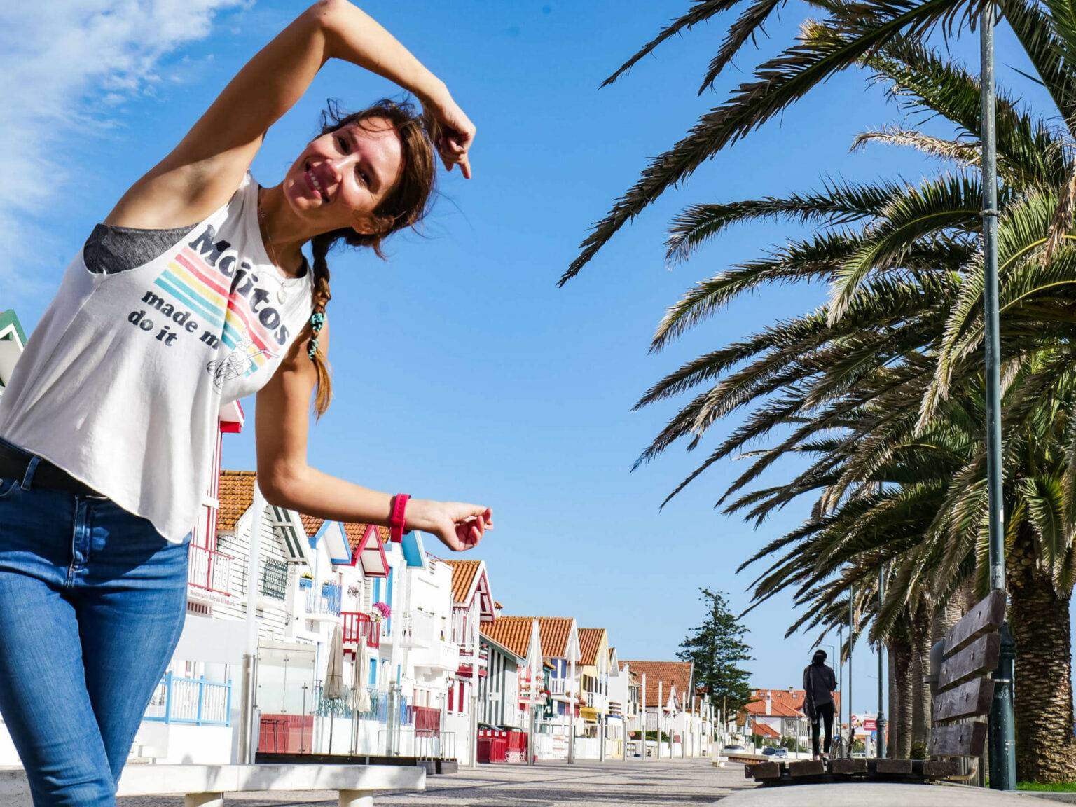 Reisebloggerin Anja Knorr lächelt vor einer bunten portugiesischen Häuserfassade und Palmen in die Kamera - das Zentrum Portugals eignet sich ideal zum Reisen allein.