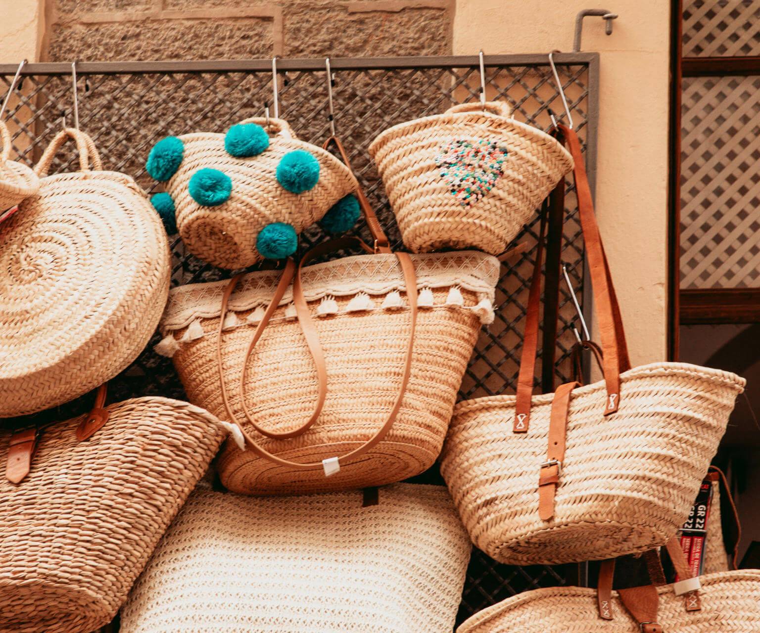 Mehrere Strohtaschen verschiedener Größen und Designs, die an einem Gitter zum Verkauf im Alameda Shop hängen, laden zum Shoppen in Sóller auf Mallorca ein.