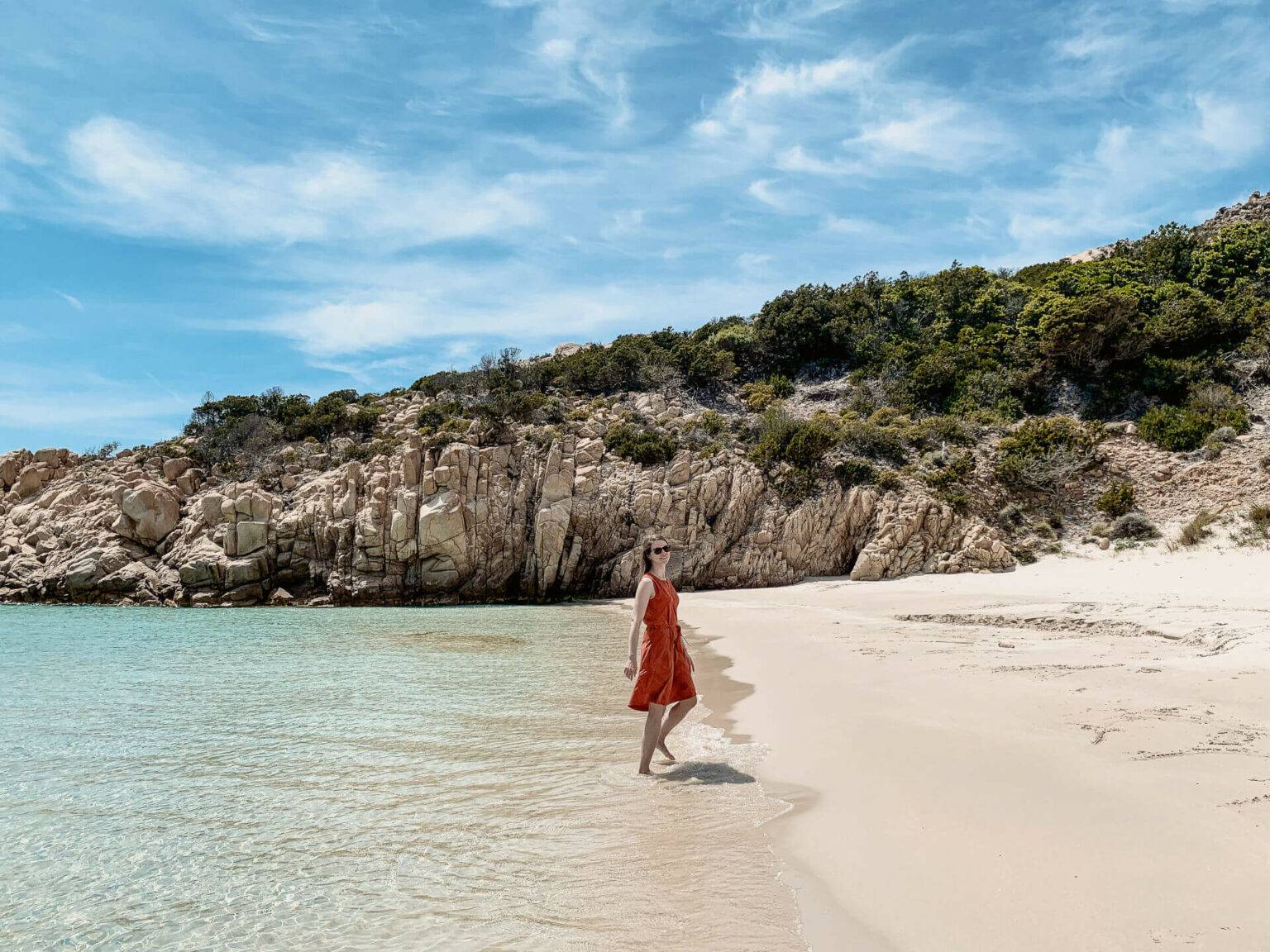 Franzi Reichelt von Coconutsports spaziert vor den Felsen am Strand der Cala Corsara auf Sardinien.