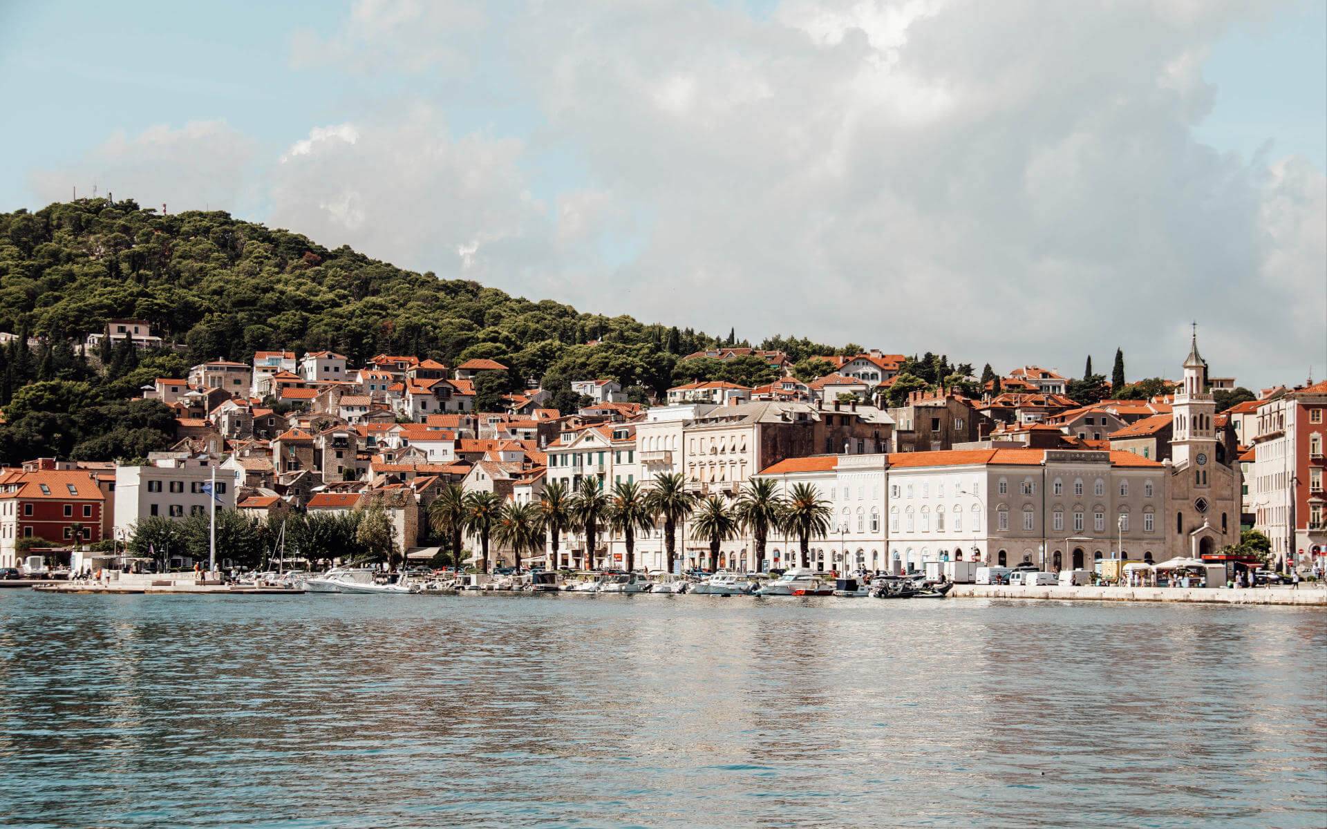 Blick über das Meer auf die mit Palmen gesäumte Uferpromenade der Altstadt von Split.