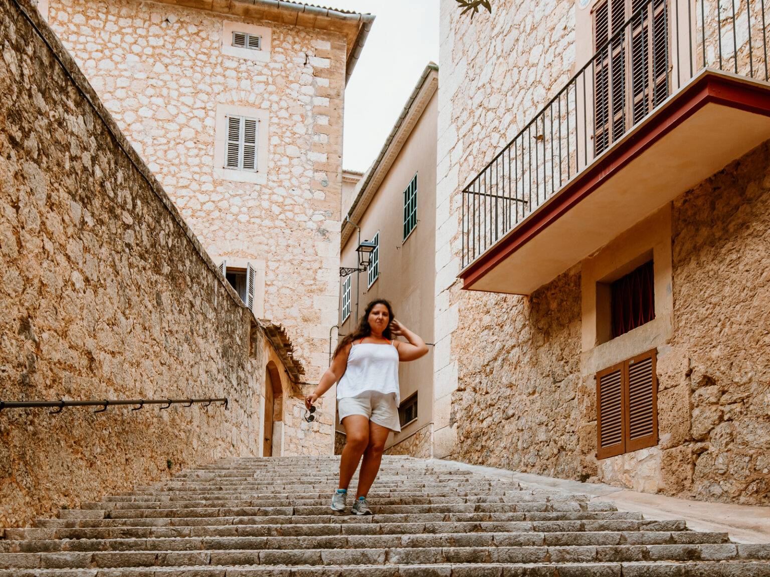 Eine Frau läuft auf einem aus Natursteinen geebneten Weg vorbei an breiten Balkonen in einem mallorquinischen Dorf.
