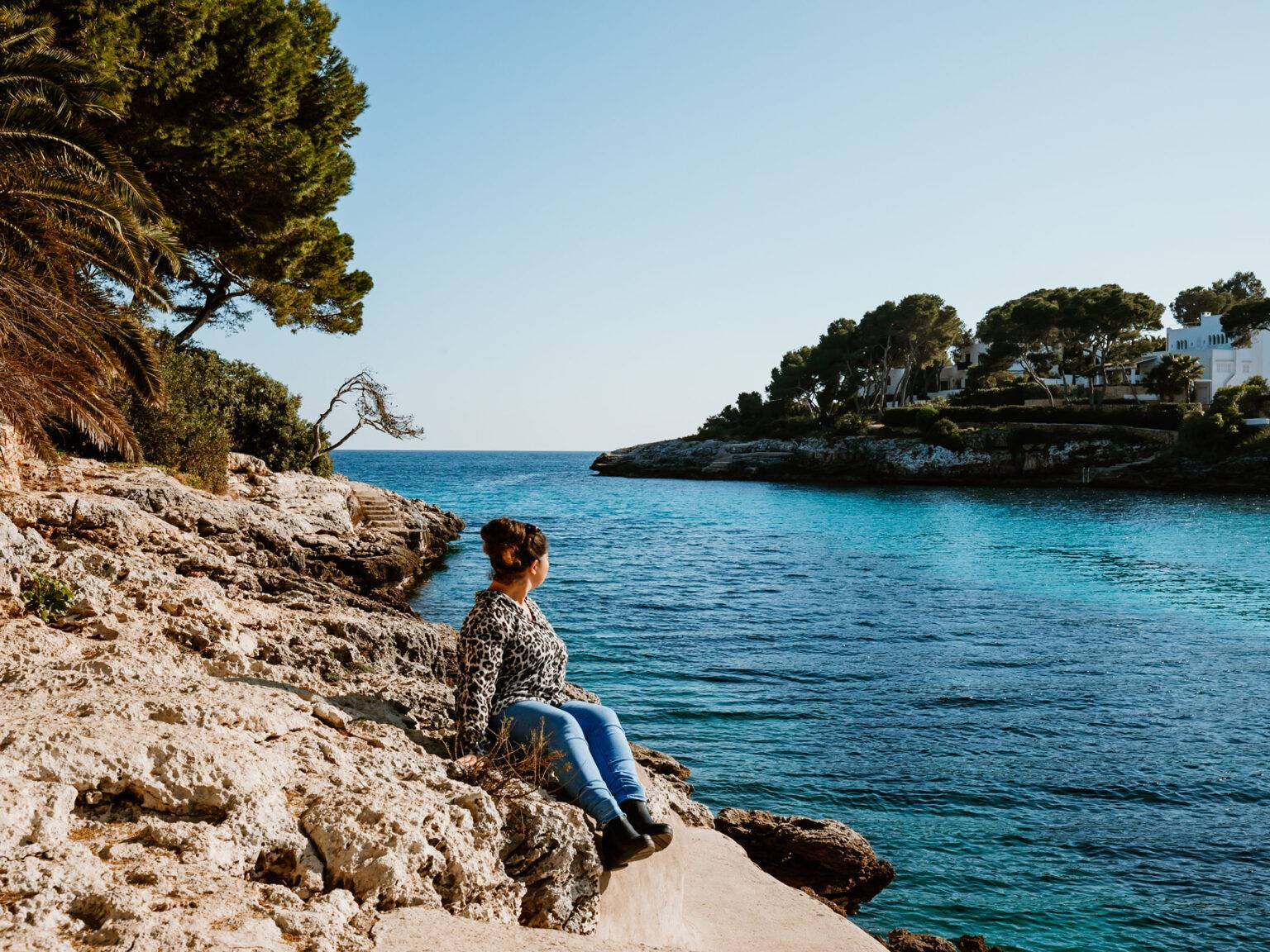 Eine Frau sitzt an einer Steinküste von Mallorca mit Blick aufs Meer
