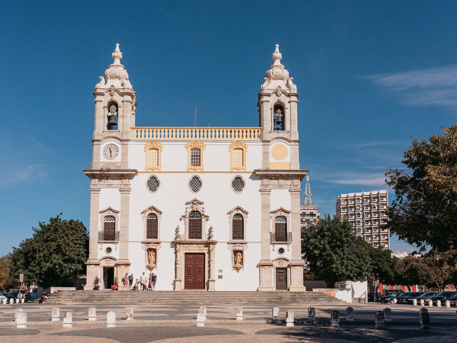 Die barocke weißfarbene Kirche "Igreja do Carmo" mit 2 Türmen in Faro ragt in den blauen Himmel.