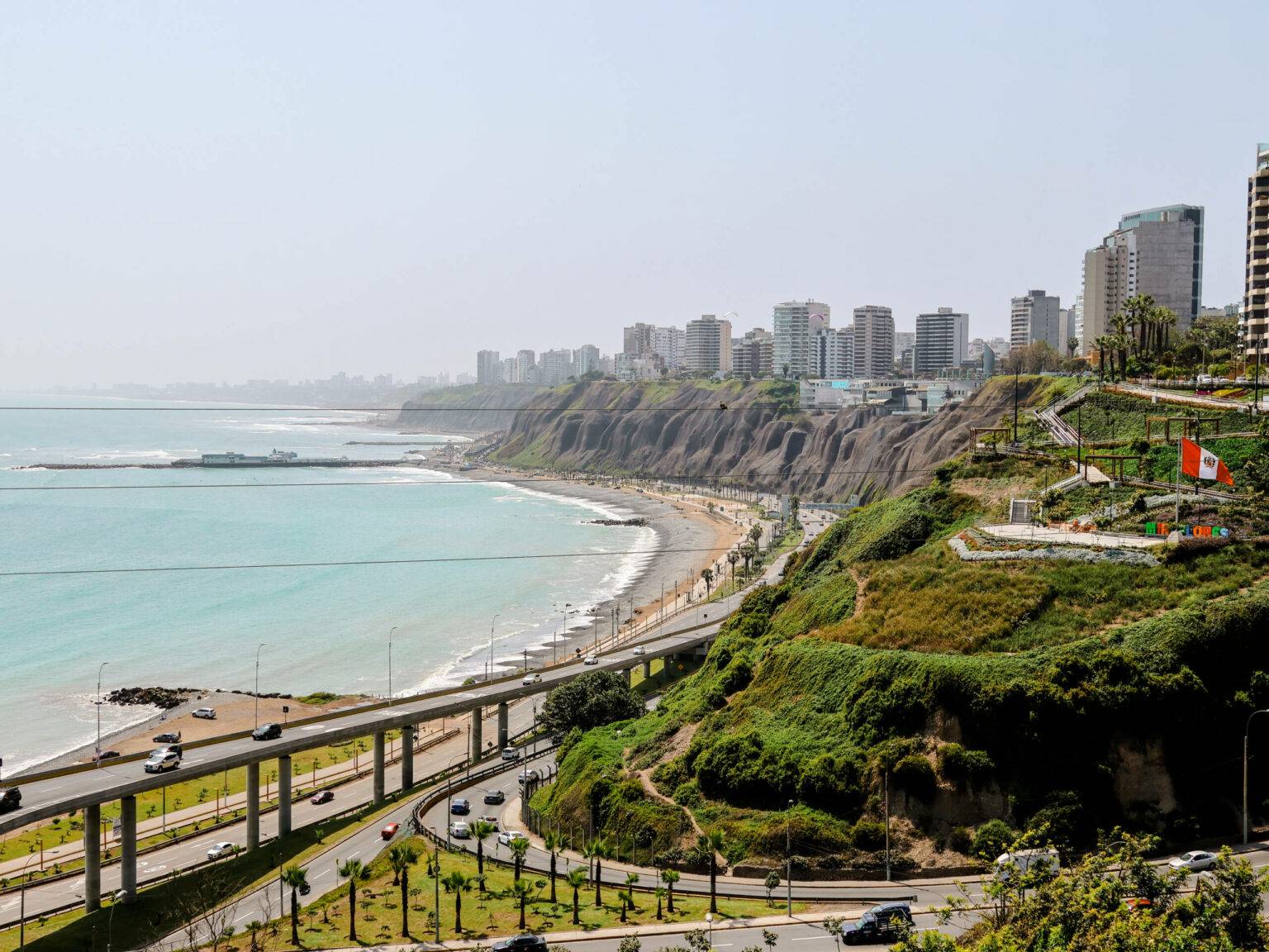 Eine lange Küste mit Strand, Straßen und begrünten Hügeln erstreckt sich in Lima.