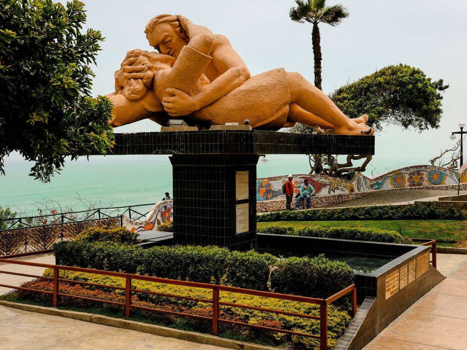 Eine Statue zweier sich küssender Menschen in Limas Park der Liebenden mit türkisfarbenem Meer im Hintergrund.